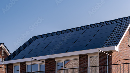 Newly build houses with solar panels attached on the roof against a sunny sky Close up of new building with black solar panels. Zonnepanelen, Zonne energie, Translation: Solar panel, , Sun Energy.  photo