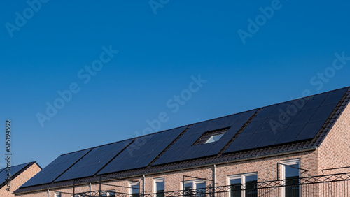 Newly build houses with solar panels attached on the roof against a sunny sky Close up of new building with black solar panels. Zonnepanelen, Zonne energie, Translation: Solar panel, , Sun Energy.  photo