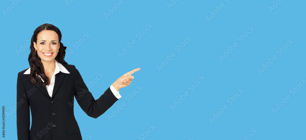 Happy smiling attractive woman in black confident suit, pointing at copy space area. Business concept. Isolated on blue background. Brunette businesswoman. Wide. Happy smiling attractive woman in black confident suit, pointing at copy space area. Business concept. Isolated on blue background. Brunette businesswoman. Wide.