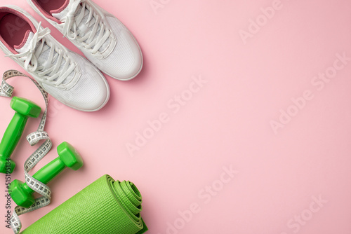 Sports concept. Top view photo of white sneakers tape measure green exercise mat and dumbbells on isolated pastel pink background with copyspace
