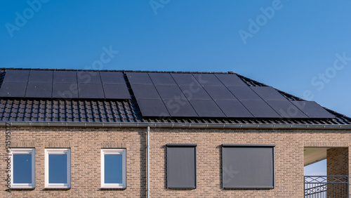 Newly build houses with solar panels attached on the roof against a sunny sky Close up of new building with black solar panels. Zonnepanelen, Zonne energie, Translation: Solar panel, , Sun Energy.  photo