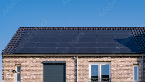 Newly build houses with solar panels attached on the roof against a sunny sky Close up of new building with black solar panels. Zonnepanelen, Zonne energie, Translation: Solar panel, , Sun Energy.  photo