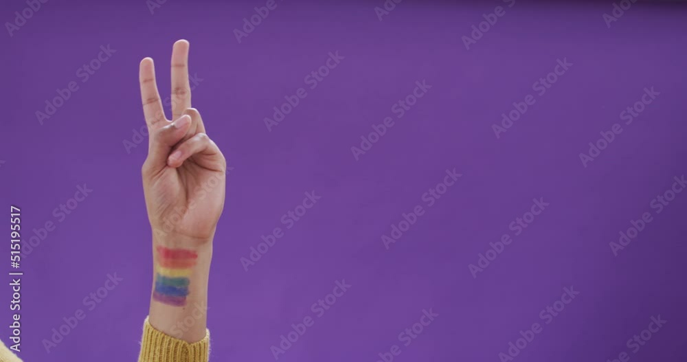 Hand of biracial man with lgbt flag on arm on purple background