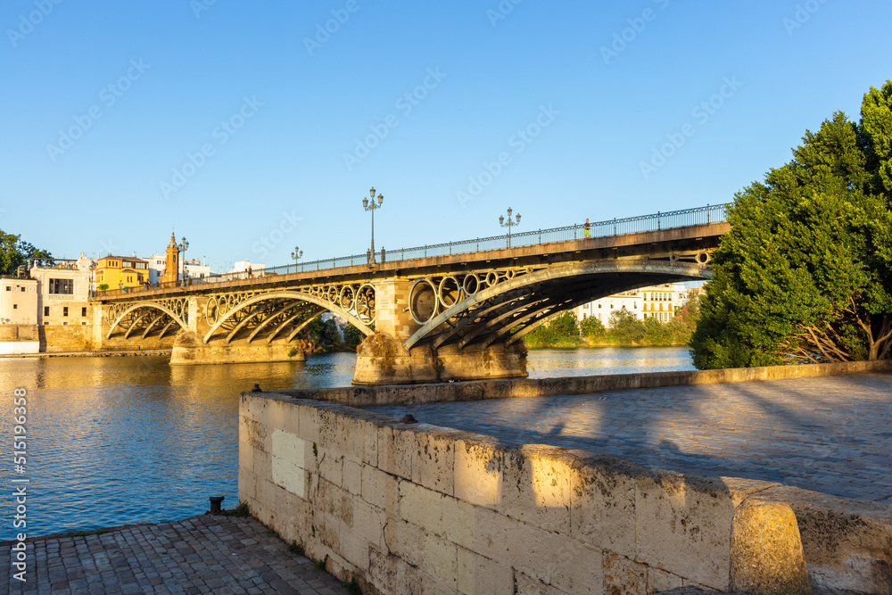 Seville, Spain, September 11, 2021: The Puente de Triana bridge over the Guadalquivir River. A historic iron arch bridge was completed in 1852, connecting the Triana neighborhood to Seville's center. Seville, Spain, September 11, 2021: The Puente de Triana bridge over the Guadalquivir River. A historic iron arch bridge was completed in 1852, connecting the Triana neighborhood to Seville's center.