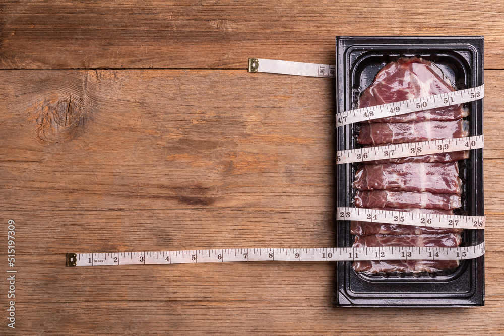Pack of raw sliced Dry Aged beef in black plastic tray and waist tape on wooden table background. Food and healthcare concept - obrazy, fototapety, plakaty 