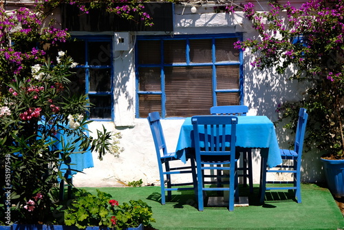 Blue dining table and chairs in front of the Mediterranean house. Garden background with bougainvillea flowers.