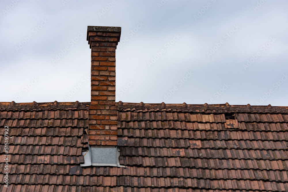 Bricks chimney on the roof with old weathered tiles that needs to be restored