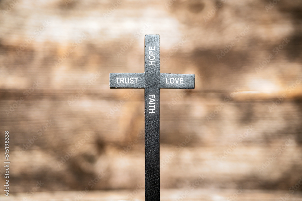 trust hope love faith text on black wooden cross with wooden blurred out background. jesus and religion concept.