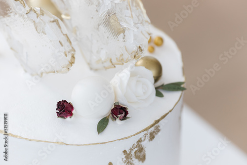 An elongated modern white wedding cake covered in cream and gold. Transparent heart-shaped lollipops. Artistic decoration.Image for menu or catalog of pastry shop.