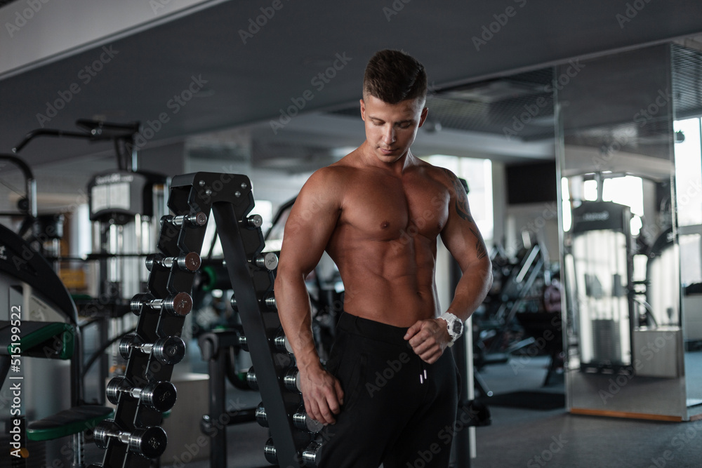 Strong sexual handsome young man model with a bare muscular torso working out in the gym
