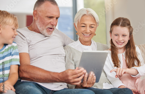 A happy mature couple bonding with their grandchildren while babysitting and using a digital tablet at home. Grandparents relaxing with their cute little grandson and granddaughter browsing internet