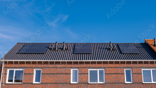 Newly build houses with solar panels attached on the roof against a sunny sky Close up of new building with black solar panels. Zonnepanelen, Zonne energie, Translation: Solar panel, , Sun Energy.  photo