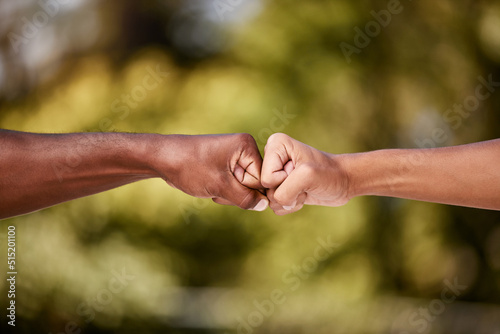 Fist bump of two interracial men outdoor against a blur background. Closeup of diverse athletes doing social gesture greeting in a park. Showing solidarity, friendship, brotherhood, teamwork or unity © Beaunitta V W/peopleimages.com