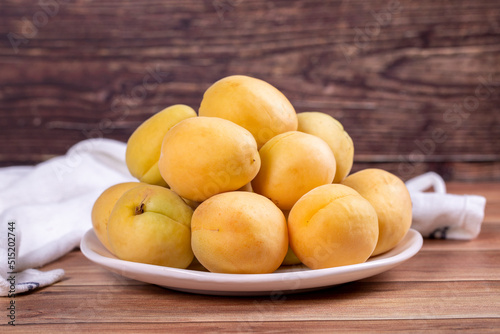 Apricots on wood background. Pile of fresh apricots in a white plate. close up