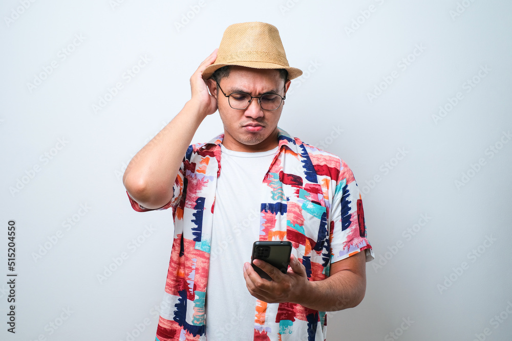 Portrait of unhappy Asian man in casual beach shirt holding mobile phone with sad expression on face while scratching his head. Portrait of unhappy Asian man in casual beach shirt holding mobile phone with sad expression on face while scratching his head.