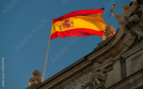 Flag of Spain winding in sunset light against blue sky on top of Royal Palace building from Madrid.