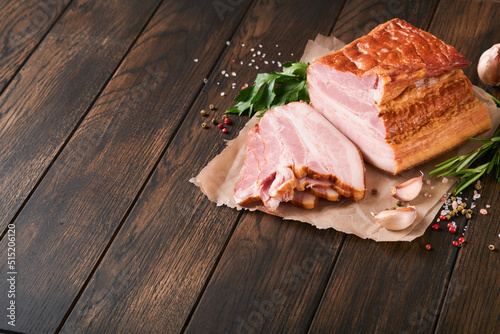 Whole Smoked Slab Bacon. Brisket. Sliced smoked gammon on a wooden table with rosemary, parsley, pepper, salt, and garlic on wooden stand and old table. Copy space. photo
