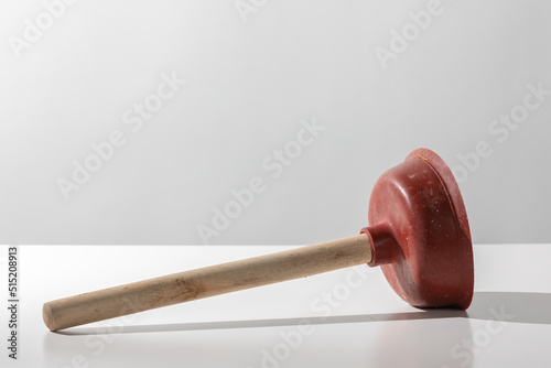 Old used red toilet plunger with wooden handle on a white background