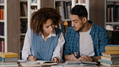 Students do homework in library teamwork working on joint project cute girl explaining task to male friend write notes preparing for exam communicate rejoice in achievement successful cooperation