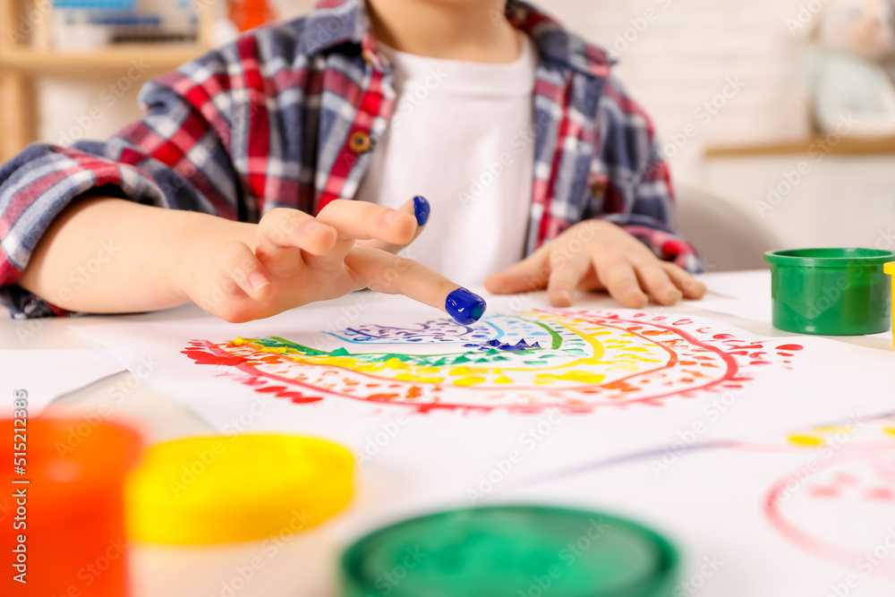 Fototapeta premium Little boy painting with finger at white table indoors, closeup