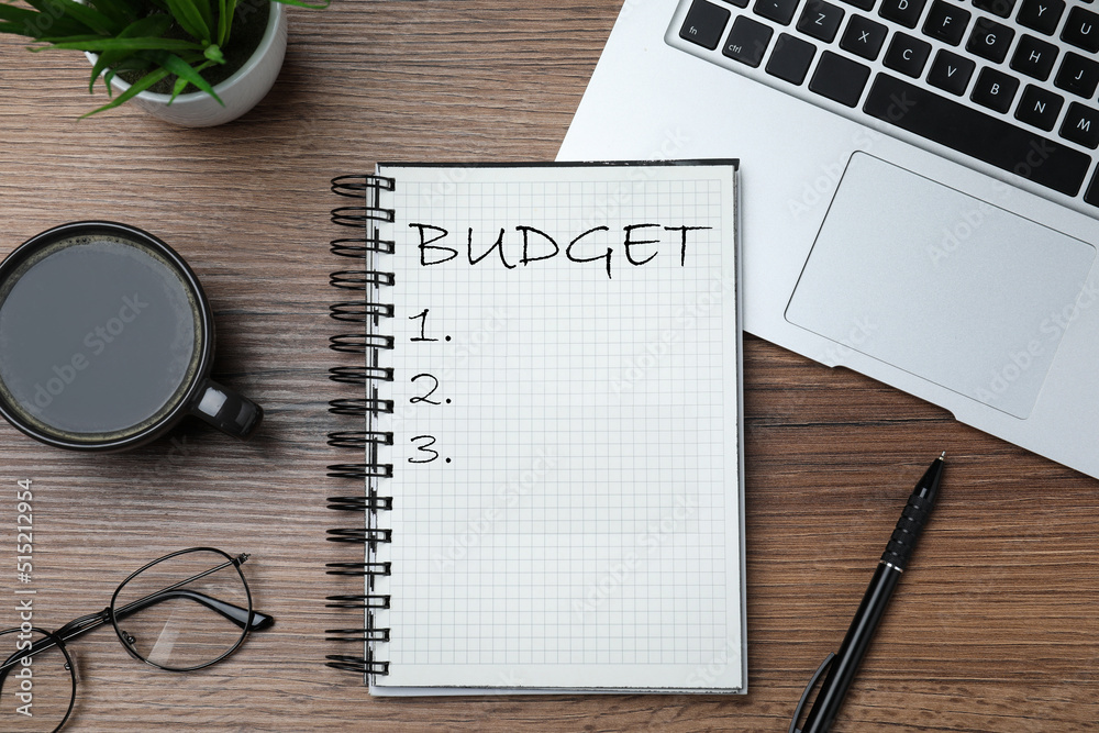 Notebook with word Budget, laptop and cup of coffee on wooden desk, flat lay Notebook with word Budget, laptop and cup of coffee on wooden desk, flat lay