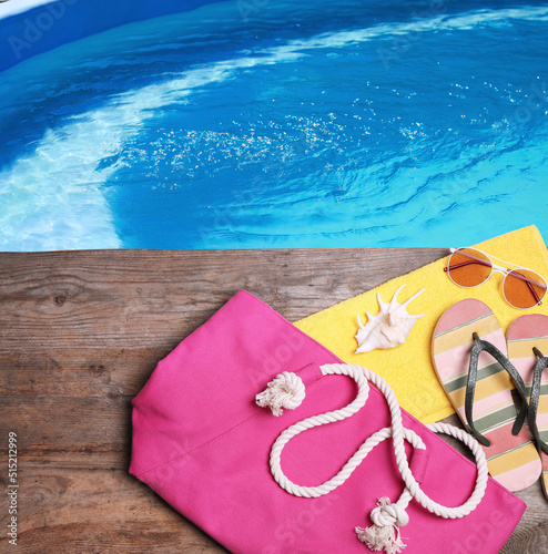 Different stylish beach accessories on wooden surface near swimming pool, above view