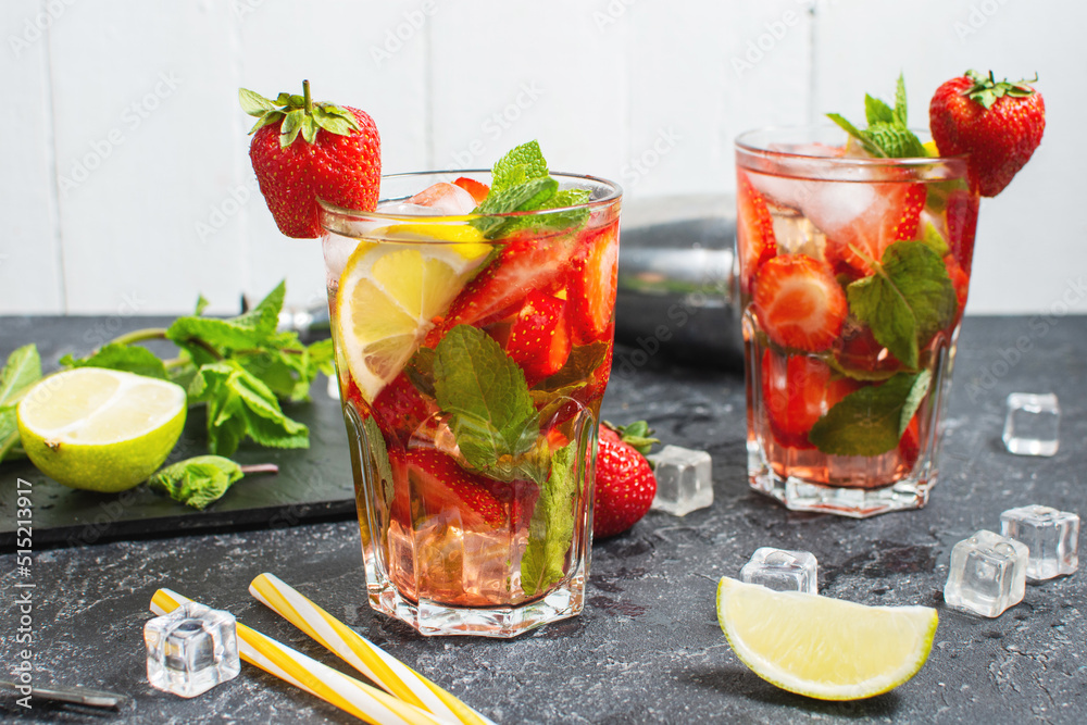 Summer refreshing mojito cocktail with strawberry, mint and lime with shaker for whipping drinks on a dark stone table