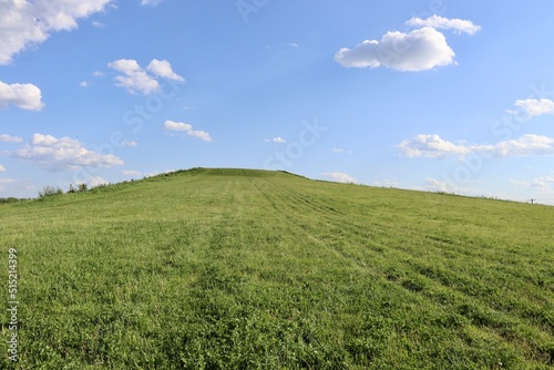 The green grass hill with the clouds in the blue sky.