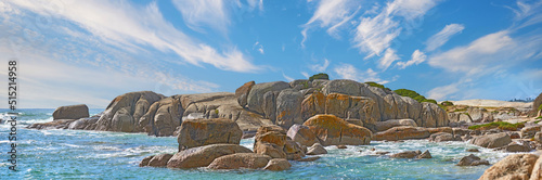 Panorama sea view of Camps Bay, Cape Town, South Africa with boulders, rocks and blue sky with copy space. Oceans waves washing onto a rough, rocky beach shore. Travel and tourism overseas and abroad