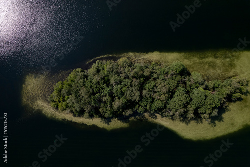 Sunspot reflection in the water of green island top down aerial view in IJzeren Man lake full of trees with sand deposit sediment surrounding it seen just below the surface of the water