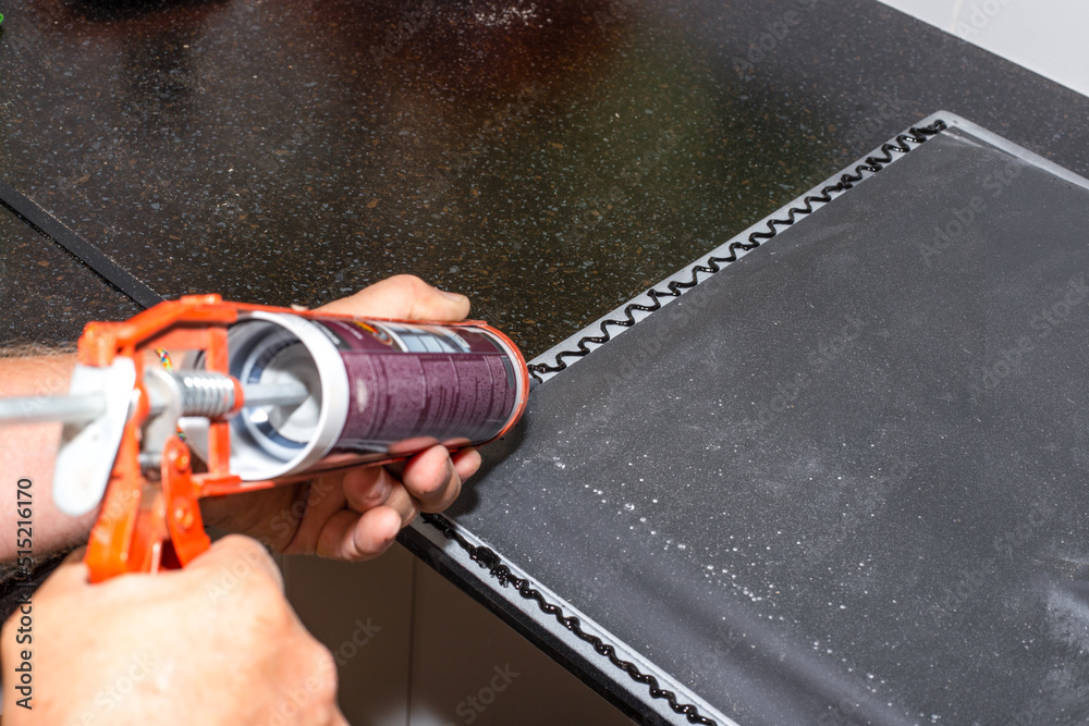 Applying black sanitary sealant with a nail gun to the edge of the