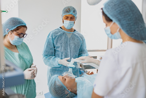 Doctor anesthesiologist holding breathing mask on patient face during operation photo
