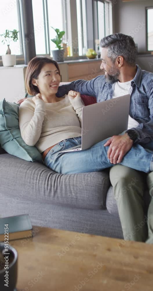Vertical video of happy diverse couple talking and using laptop Vertical video of happy diverse couple talking and using laptop
