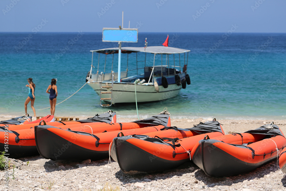 orange inflatable double kayak boats stand in a row on the seashore Close-up of boats and azure water in the background