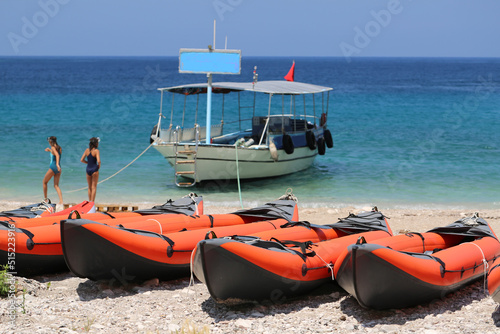 orange inflatable double kayak boats stand in a row on the seashore   Close-up of boats and azure water in the background