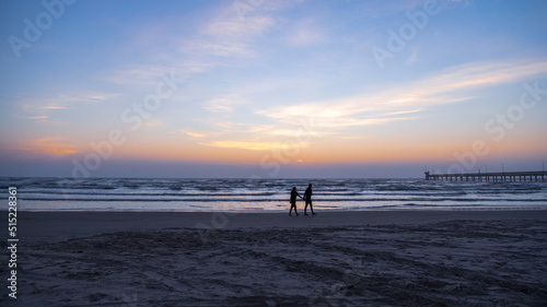 Silhouetted couple walking on the beach in the early morning just before sunrise 