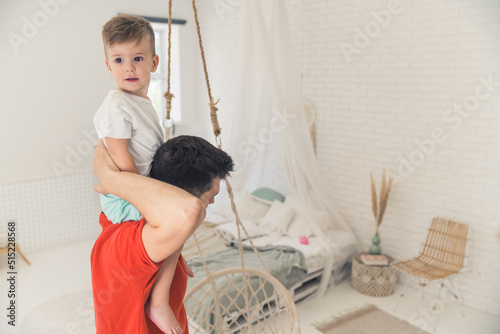little Caucasian boy riding his father's neck in the living room, fatherhood concept. High quality photo