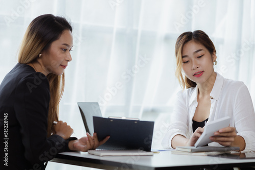 Atmosphere in the office of a startup company, two female employees are discussing, brainstorming ideas to working on summaries and marketing plans to increase sales and prepare reports to managers.
