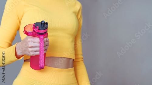Fit woman with orange outfit holding pink water bottle. Fitness woman drinking water during workout .Hydration during training concept 