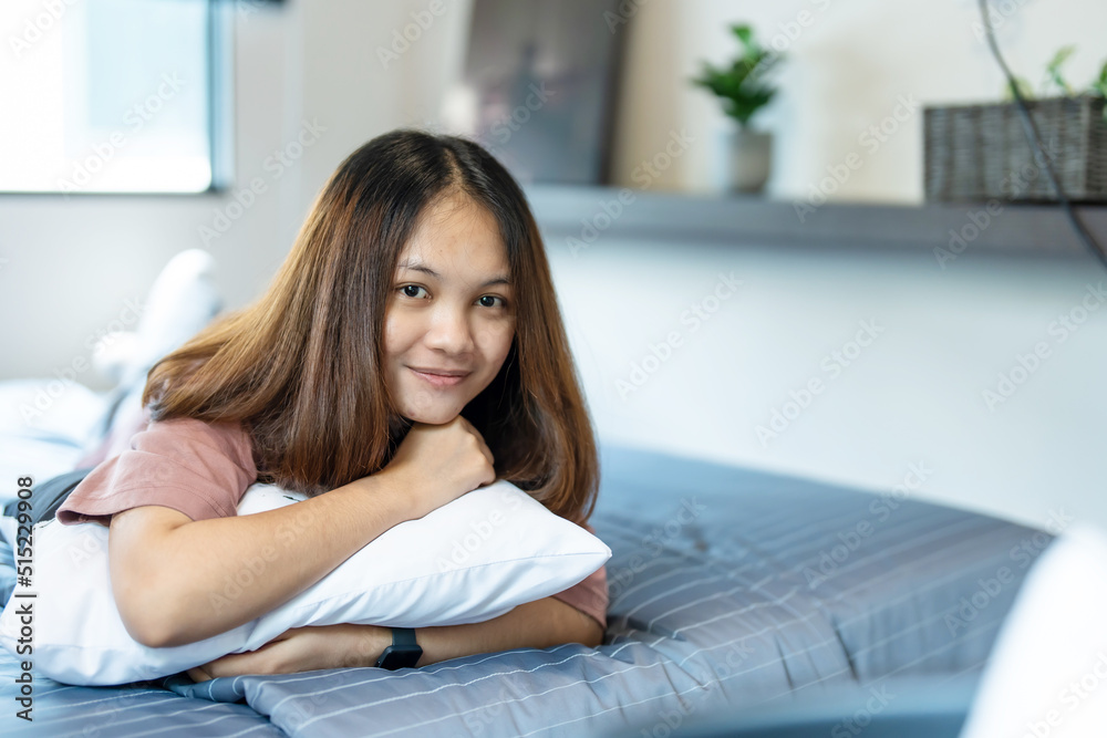 A teenage long-haired Asian woman lies in bed with a happy smile on her face and looks at the camera in her bedroom. A teenage long-haired Asian woman lies in bed with a happy smile on her face and looks at the camera in her bedroom.