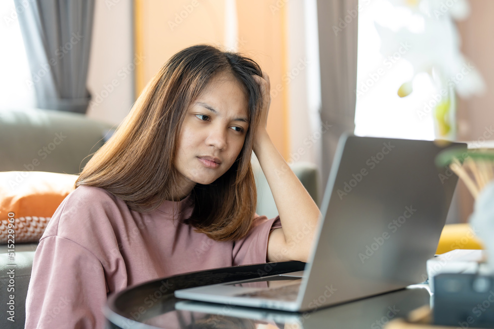 young Asian woman is studying online in front of her laptop computer and typing a message. She showed signs of thinking by using her left hand to support her hold. Work from home. young Asian woman is studying online in front of her laptop computer and typing a message. She showed signs of thinking by using her left hand to support her hold. Work from home.