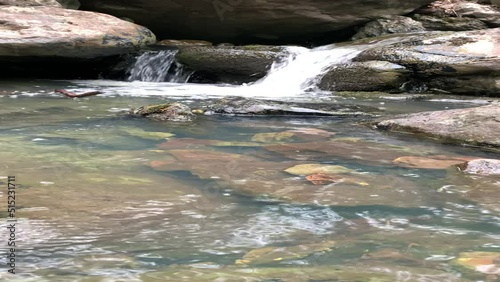 Mountain river - a small waterfall on a river with crystal clear water that flows among gray stones in a green forest on a cloudy summer day. Big stones near the pond