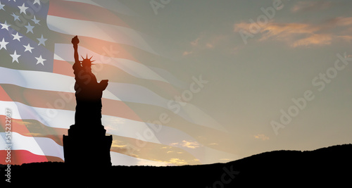 Statue of Liberty with a large american flag and sunset sky on background.