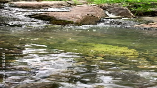 Mountain river - a small waterfall on a river with crystal clear water that flows among gray stones in a green forest on a cloudy summer day. Close up of a rock next to a body of water