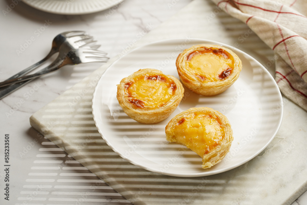 Traditional portuguese vanilla pudding puff pastry pastel de nata on white plate on marble board with a cup of coffee in white porcelain Traditional portuguese vanilla pudding puff pastry pastel de nata on white plate on marble board with a cup of coffee in white porcelain