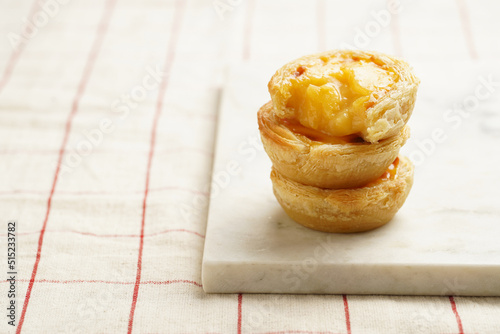 Traditional portuguese vanilla pudding puff pastry pastel de nata stacked on each other on marble board on checkered table cloth