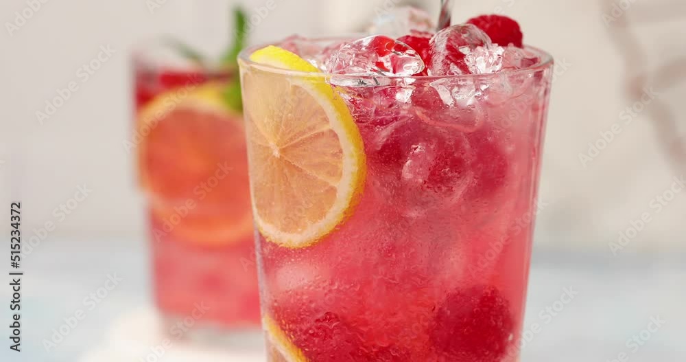 Spring or summer refreshing cold cocktail or mocktail with berries and lemon, raspberry lemonade being stirred with a spoon