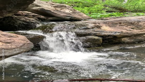 Mountain river - a small waterfall on a river with crystal clear water that flows among gray stones in a green forest on a cloudy summer day. Big stones near the pond