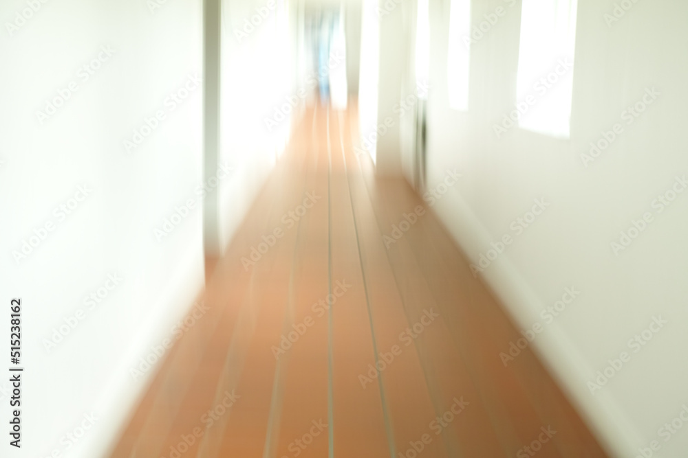 A blurry tiled hallway with white walls and sun shining through the open windows. An empty hospital, clinic or school corridor A blurry tiled hallway with white walls and sun shining through the open windows. An empty hospital, clinic or school corridor