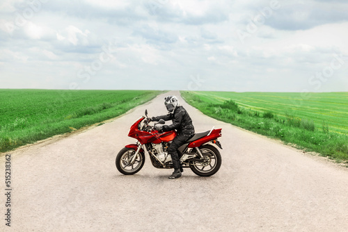 The motorcyclist stands in place with the motorcycle in the middle of the country road and looks at the camera